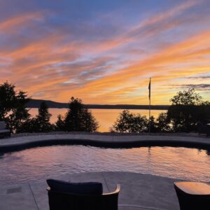 A pool with chairs and a sunset in the background.