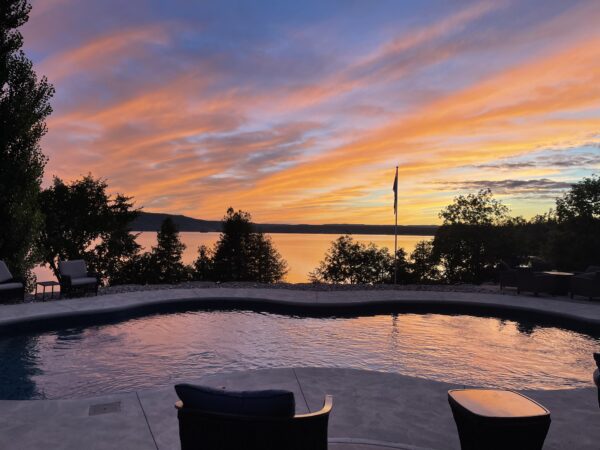 A pool with chairs and a sunset in the background.